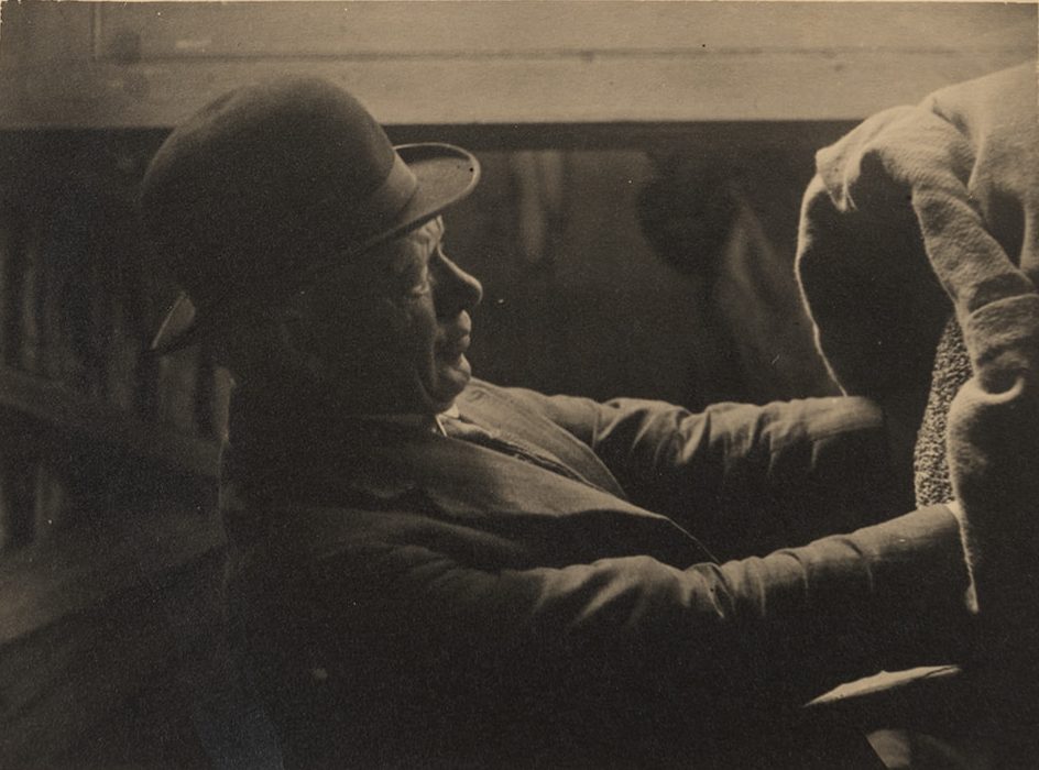Black and white photo of man in bowler had with hands in sack of grain