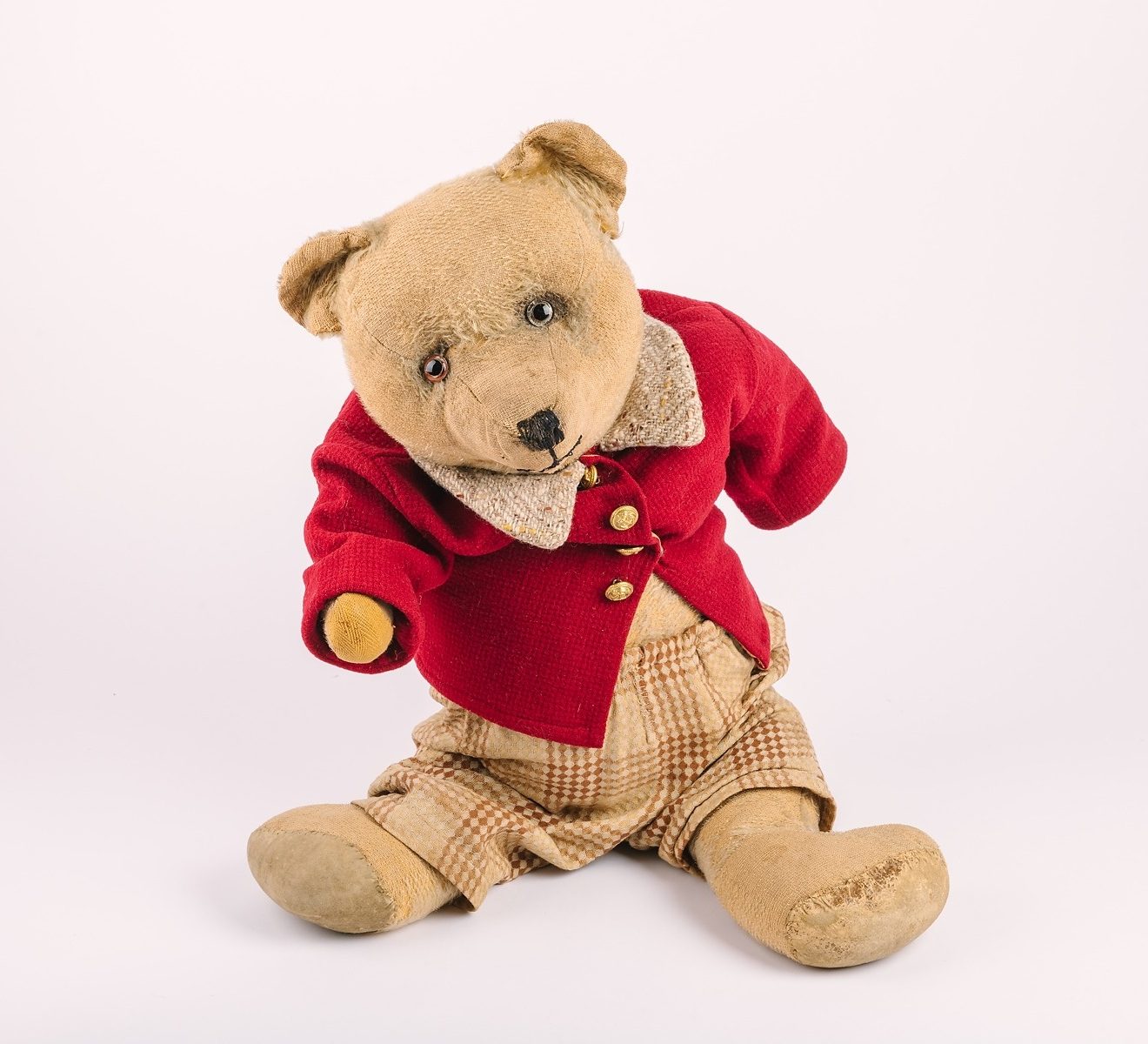 Teddy bear wearing red buttoned up jacket and tweed trousers