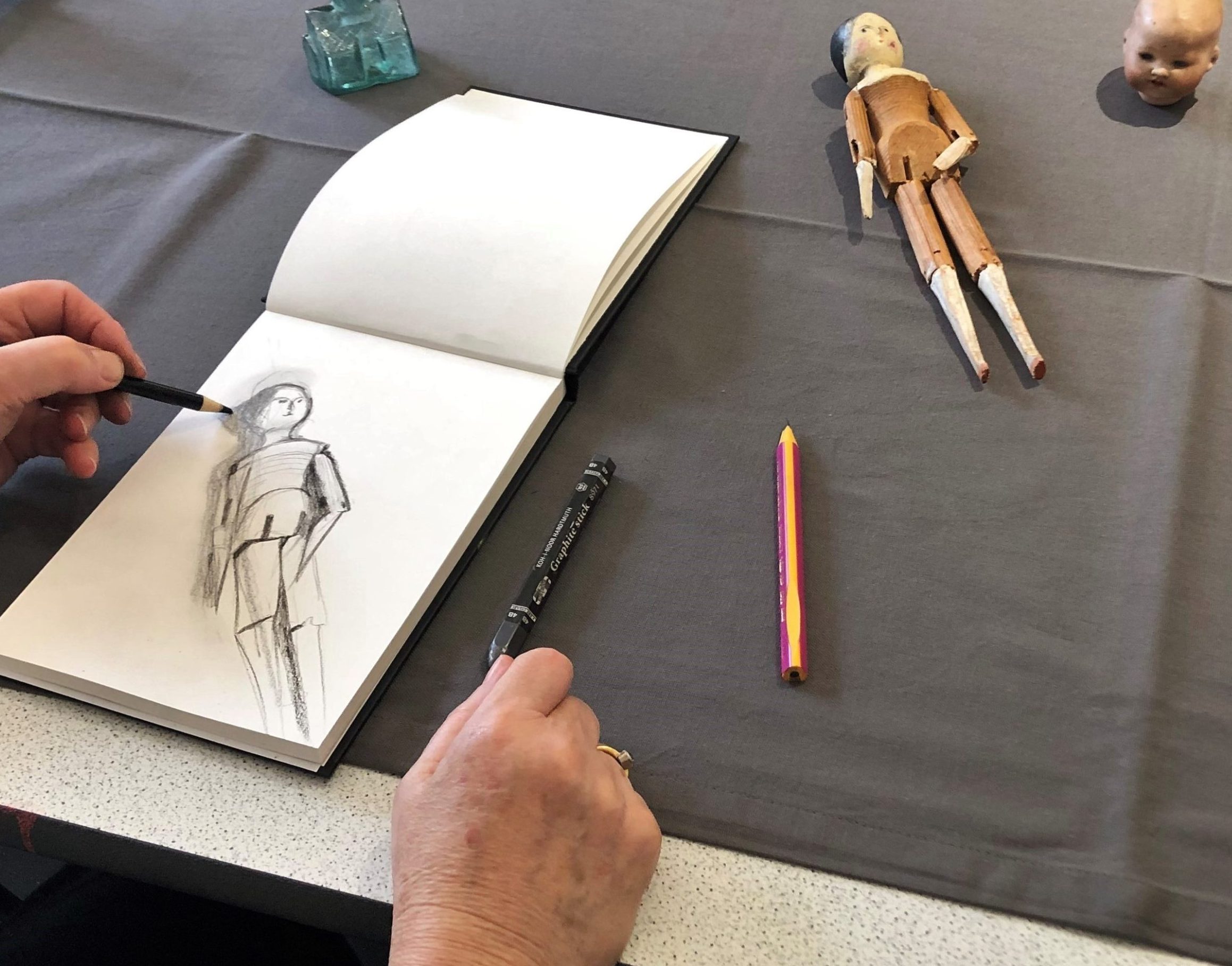 Hands drawing a wooden doll on table in front